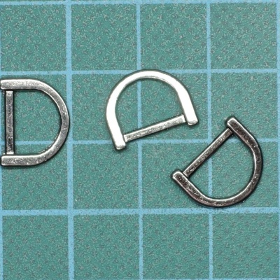 Três argolas de metal em forma de D sobre uma superfície quadriculada verde.