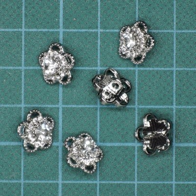 Botões florais prateados com pedras sobre superfície quadriculada verde