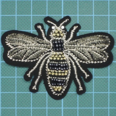 Aplicação bordada em forma de abelha com fundo preto sobre grelha azul