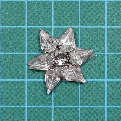 Broche em forma de estrela com pedras transparentes em fundo verde quadriculado