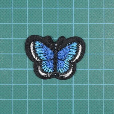 Patch bordado em forma de borboleta azul colocado sobre superfície quadriculada verde