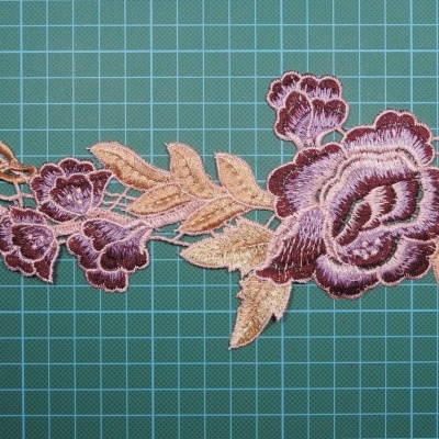 Aplicação em renda bordada floral roxo e bege sobre superfície verde quadriculada