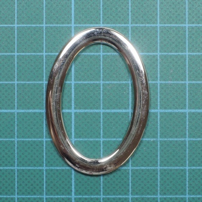 Anel oval metálico prateado sobre base quadriculada verde