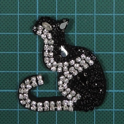 Broche de gato em cristais brilhantes preto e branco sobre fundo azul com grelha