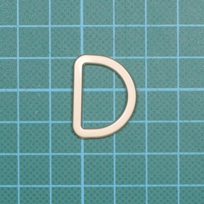 Argola em forma de D bege sobre superfície quadriculada de corte