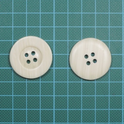 Dois botões redondos bege claro em tapete de corte verde com grelha