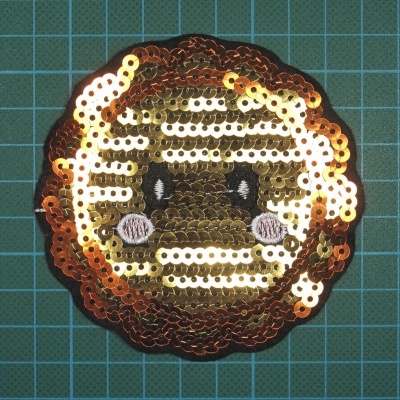 Patch redondo com emoji brilhante em fundo quadriculado verde.