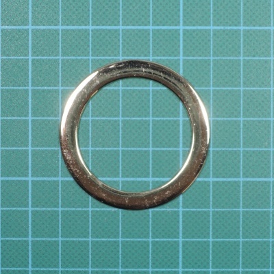 Anel metálico prateado redondo sobre superfície quadriculada verde-azulada