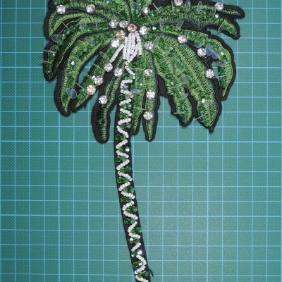 Aplicação bordada de palmeira com pérolas e pedras em fundo azul quadriculado.