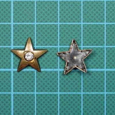 Dois botões em forma de estrela dourado e prateado sobre superfície quadriculada verde