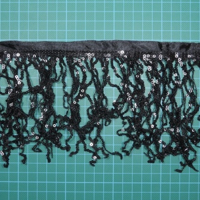 Renda preta com lantejoulas e franjas sobre superfície verde quadriculada