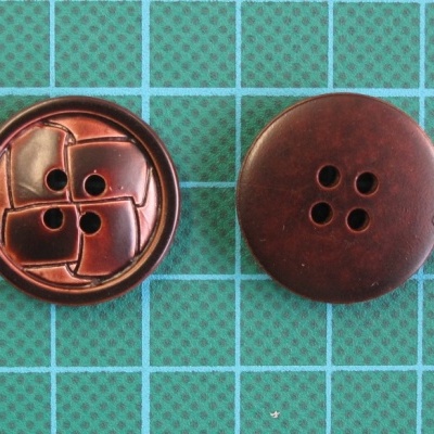 Duas botões castanhos escuros com quatro furos sobre uma superfície verde quadriculada