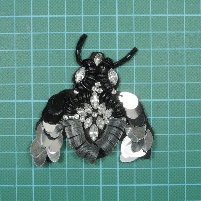 Broche de abelha em lantejoulas e cristais sobre fundo verde quadriculado