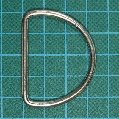 Argola D metálica prateada sobre base verde com grelha quadriculada azul