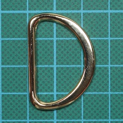 Argola em forma de D dourada sobre base quadriculada verde