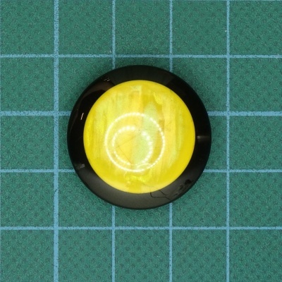 Botão redondo amarelo com borda preta sobre superfície quadriculada verde