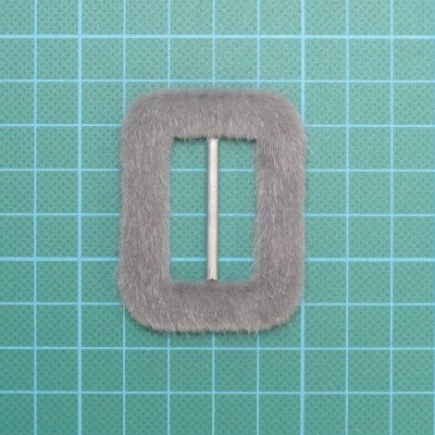 Fivela retangular cinzenta com barra metálica sobre fundo de grelha verde