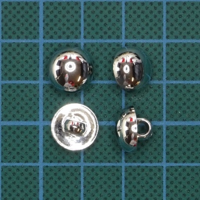 Botões metálicos redondos prateados sobre superfície verde com padrão de quadrícula