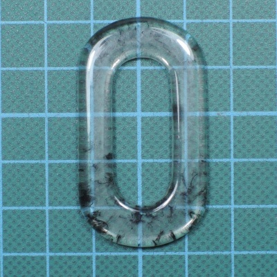 Anel oval transparente com inclusões negras sobre superfície quadriculada azul