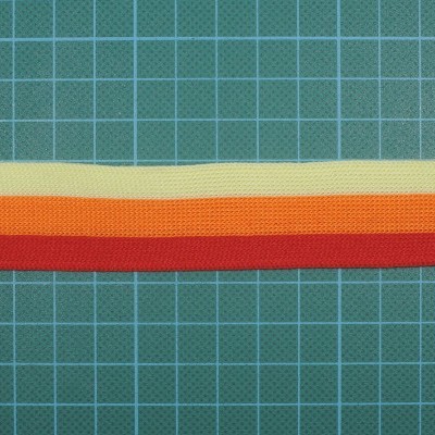 três faixas de tecido coloridas em amarelo, laranja e vermelho sobre um fundo verde com grelha branca