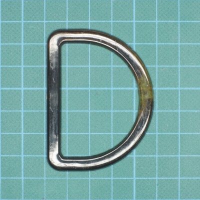 Argola metálica em forma de D sobre fundo verde quadriculado