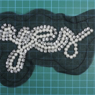 Aplique de pérolas e cristais formando a palavra 'grey' sobre base preta