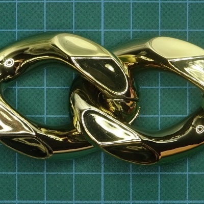 Duas peças interligadas em metal dourado sobre superfície verde com padrão de grelha