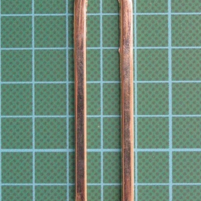 Argola oval dourada sobre superfície verde com grelha azul