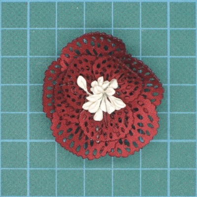 Flor artificial vermelha com detalhes brancos sobre superfície verde quadriculada