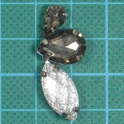 bijuteria com três pedras decorativas fumadas e prateada sobre fundo verde quadriculado