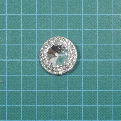 Botão redondo transparente com borda prateada brilhante em superfície verde quadriculada