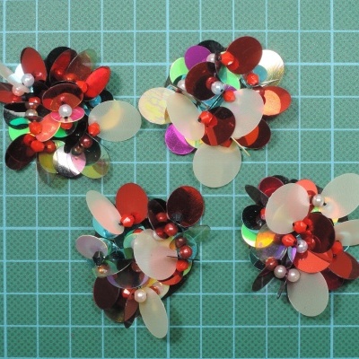 Três acessórios decorativos com lantejoulas coloridas e pérolas sobre fundo quadriculado verde