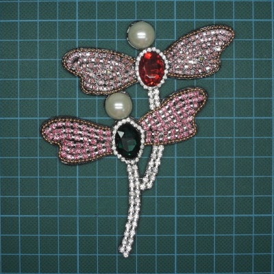 Broche com asas de borboleta em pedras coloridas sobre fundo verde quadriculado