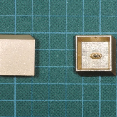 Caixa de joalharia bege com anel dourado sobre base de tecido fina, sobre superfície verde quadriculada