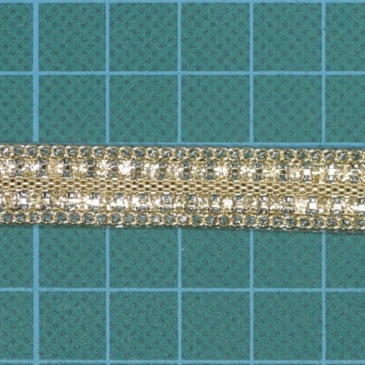 Fita decorativa dourada entrelaçada em tecido metálico sobre fundo quadriculado