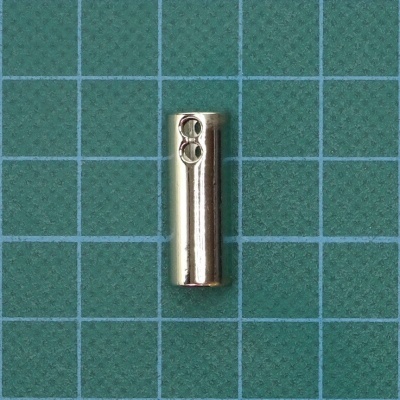 Peça metálica cilíndrica prateada sobre superfície de grade verde