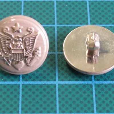 Botões metálicos dourados com águia sobre superfície azul tipo grade