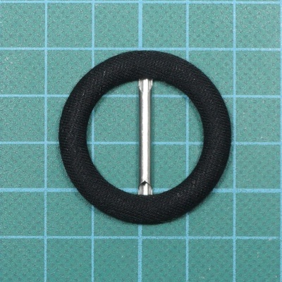 Fivela circular preta com barra metálica sobre fundo de grade azul claro