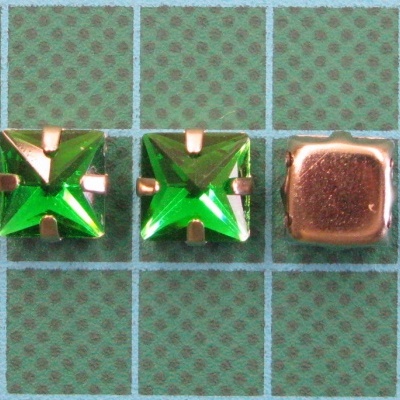 Tachas quadradas com pedra verde e base metálica dourada sobre fundo quadriculado verde