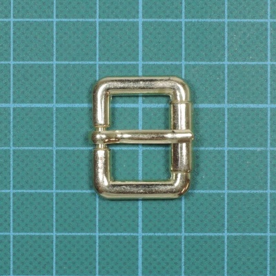 Fivela metálica dourada retangular sobre fundo verde quadriculado