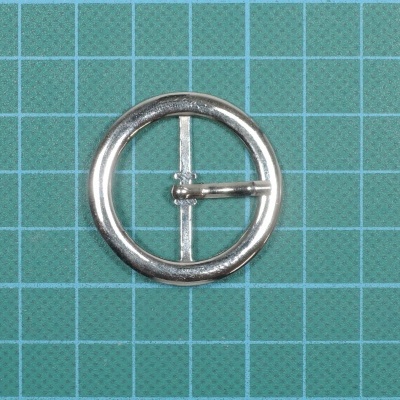 Fivela circular metálica prateada sobre fundo quadriculado azul