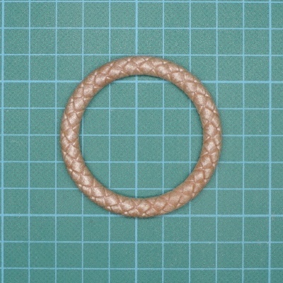 Pulseira bege trançada sobre fundo verde quadriculado.