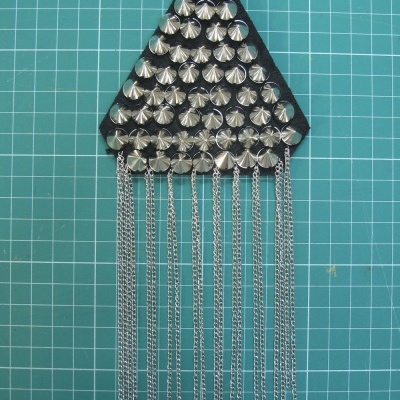 Acessório triangular preto com tachas prateadas e correntes penduradas