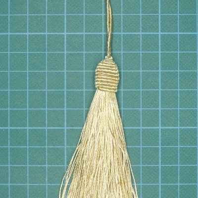 Franja decorativa bege clara com laço para pendurar sobre superfície de corte verde quadriculada azul