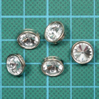 Botões transparentes com borda metálica sobre tecido verde quadriculado