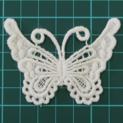 Aplicação em renda branca em forma de borboleta sobre fundo verde escuro com grelha.