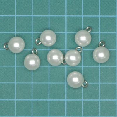 Oito pequenas pérolas brancas com argolas metálicas sobre superfície azul quadriculada