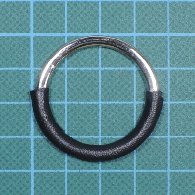 Anel metálico prateado e preto sobre superfície quadriculada verde