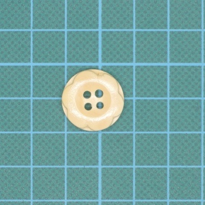 Botão redondo bege com quatro furos e relevo sobre superfície de corte azul e verde