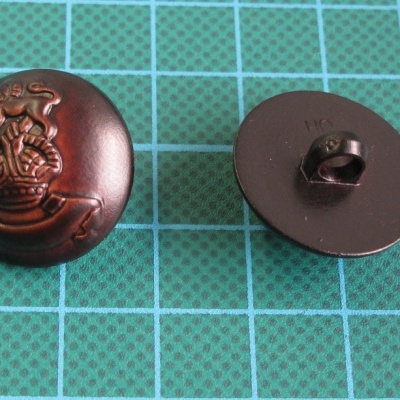 Dois botões metálicos castanho escuro com brasão em relevo sobre superfície quadriculada verde